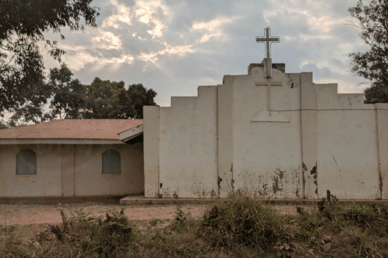 Church building with cross under cloudy sky in rural setting.