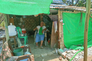 Man in wheelchair in a rural makeshift shelter with green tarps.