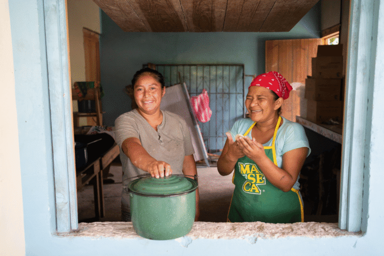 Two women smiling and serving food in a community kitchen.
