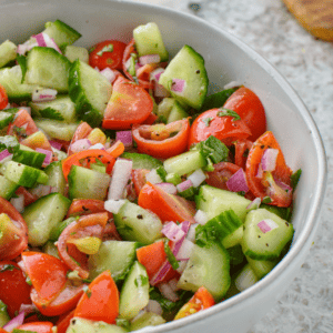 Bowl of chopped tomatoes, cucumbers, red onion, and herbs mixed together as a fresh vegetable salad.
