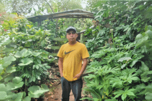 Young man in a yellow Nike t-shirt standing in lush garden.