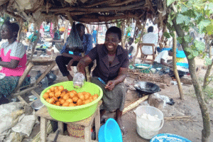 Smiling woman selling fried snacks at a community market.
