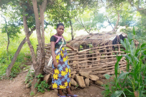 Young girl standing near a traditional hut in a rural setting.