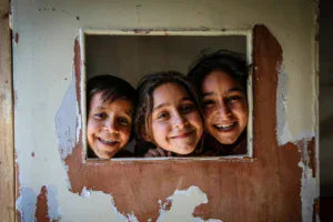 Three children look through a window opening in a community building.