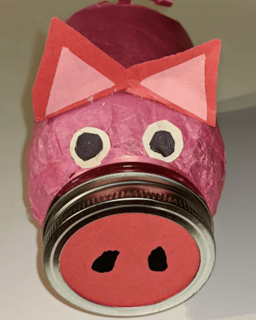 Pig-themed donation jar with paper ears and eyes for fundraising event.