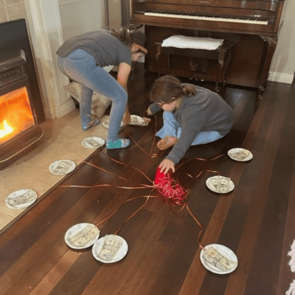 Children arranging gift packages with red ribbons on a wooden floor.