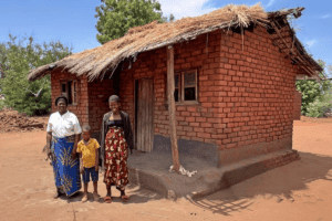 Rural community home with family outside, traditional brick and thatched roof.