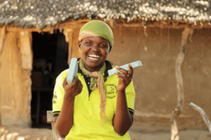 Happy woman holding soap bars in front of traditional hut in Uganda.