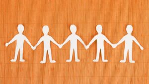 White paper cutout figures holding hands in a chain on an orange textured background.
