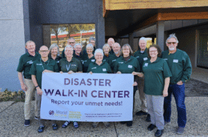 Group of volunteers holding a disaster walk-in center banner outside a building.