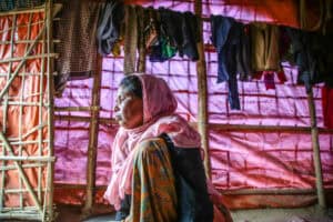 Woman sitting inside a shelter made of bamboo and fabric, looking outside thoughtfully.