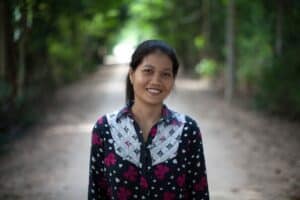 Smiling woman in a floral shirt on a rural path.