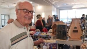 Elderly man at community event showcasing birdhouses and handmade gifts.