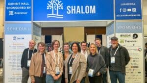 Group of conference attendees standing in front of a CCDA exhibit booth with signage and schedule board.