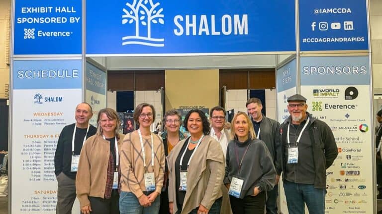 Group of conference attendees standing in front of a CCDA exhibit booth with signage and schedule board.