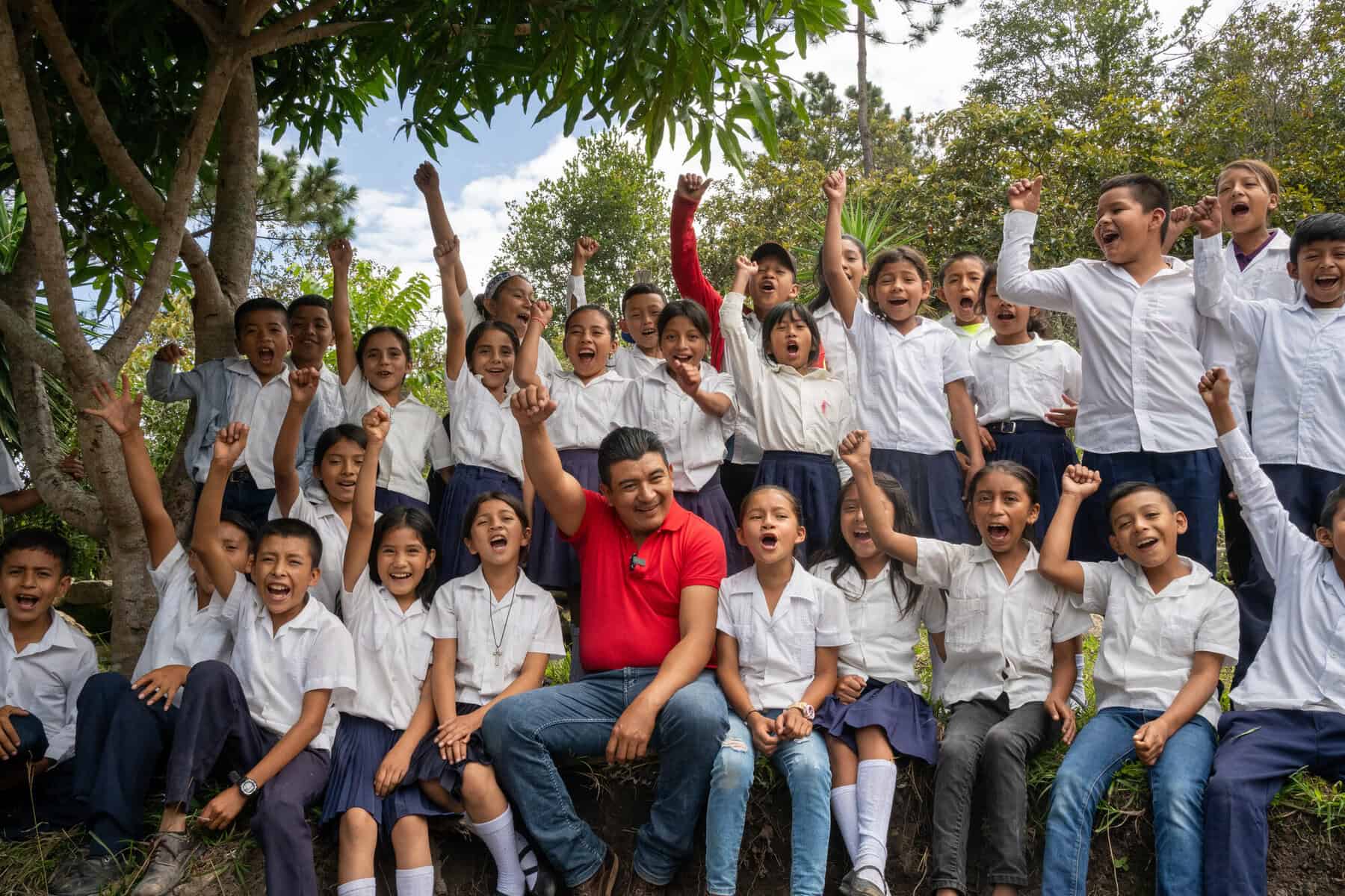 Group of happy children in school uniforms outdoors with a teacher.