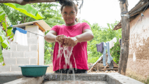 Young girl washing hands at a water source in a rural setting.