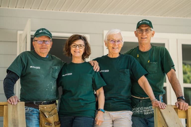 Volunteers in green shirts and hats smiling after disaster relief work.