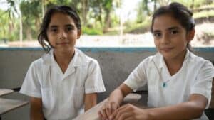 Two girls in school uniforms sitting at desk in Honduras classroom.