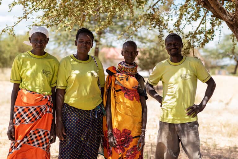 Local community leaders standing under a tree in a rural area for food security.