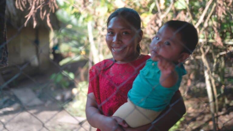 Smiling woman holding a child in a rural Guatemalan environment.