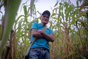 Smiling farmer standing in a cornfield with crossed arms.