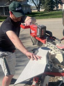 Volunteer uses a power saw to cut siding boards outdoors during home repair work.