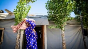 Young girl in traditional dress standing outside her home.