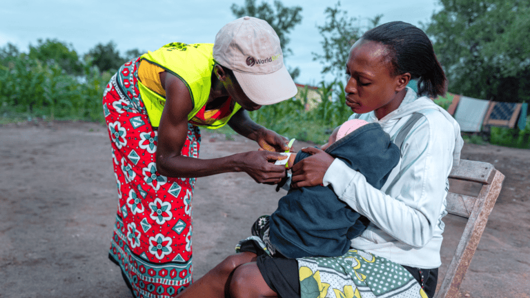 Health volunteer providing care to a mother and child outdoors in Kenya.