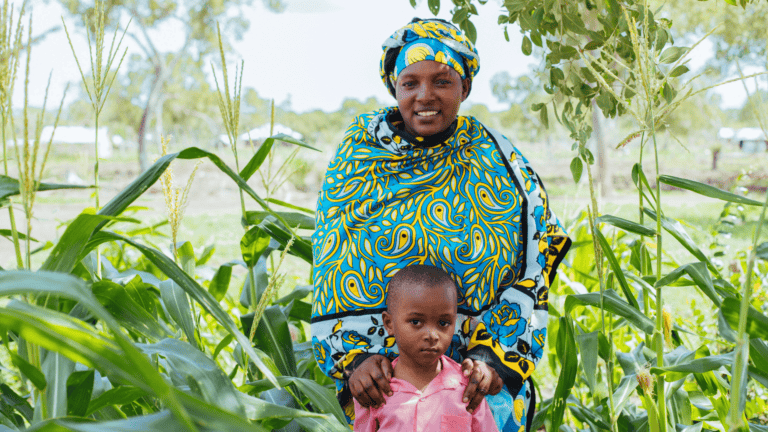Smiling woman and child in lush green garden with tall plants.