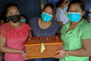 Women in Nicaragua holding a wooden box with a lock, wearing face masks.