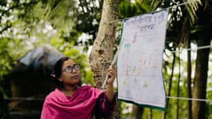 Community volunteer pointing to a health education poster during an outdoor training session in Bangladesh.