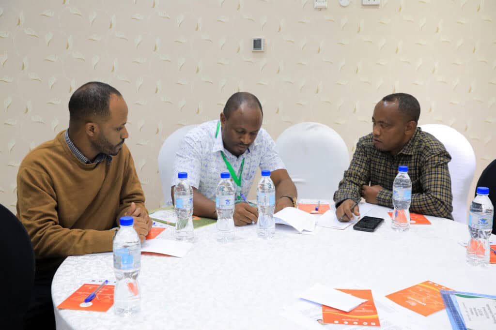 Three participants review notes and discuss ideas around a table during a conference session.