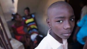 Child standing in a doorway while other people gather inside a shelter building in Haiti.