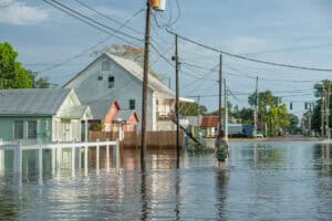 Person walking through a flooded residential street lined with homes and utility poles
