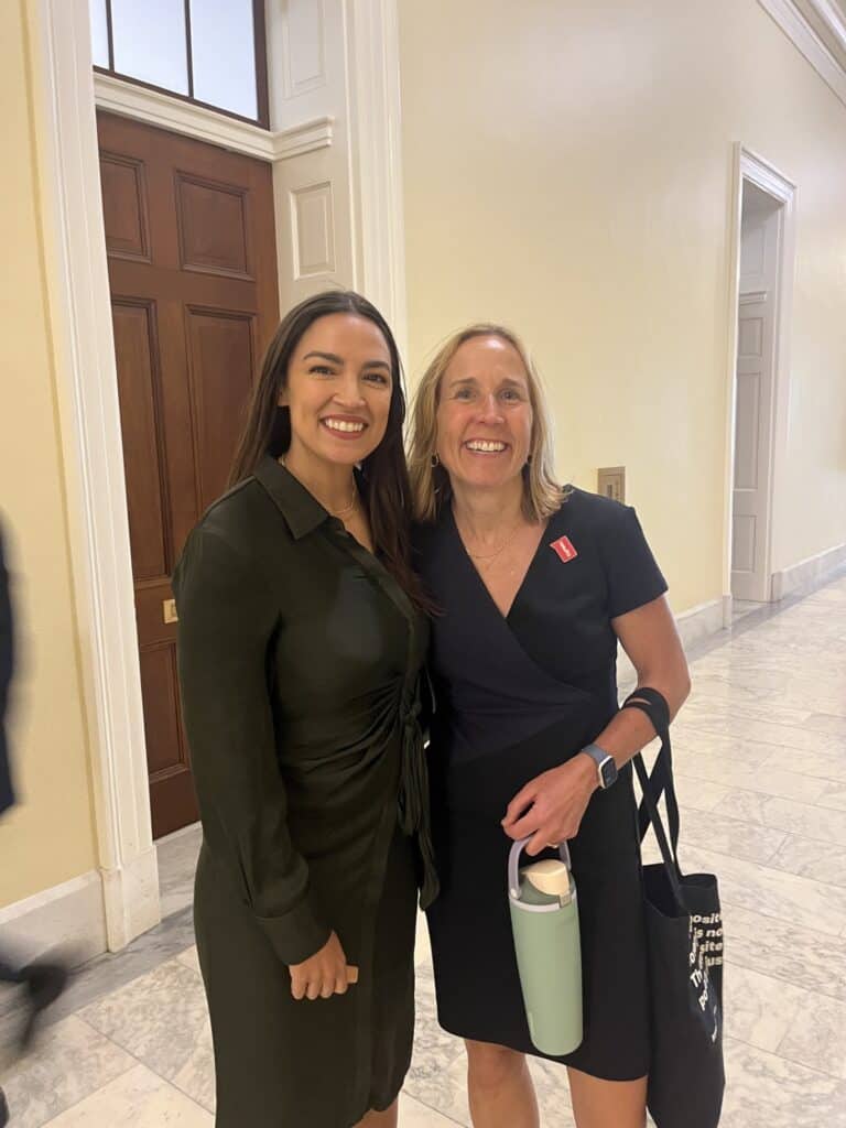 Representative Alexandria Ocasio-Cortez and Jodi Koeman smile together in a hallway on Capitol Hill.