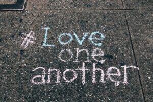 Chalk message reading “Love one another” written on a concrete sidewalk.