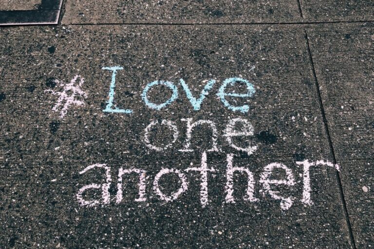 Chalk message reading “Love one another” written on a concrete sidewalk.