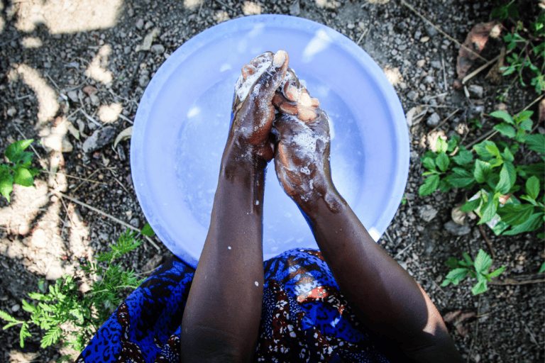 An African woman washes her hands with soap over a blue bucket