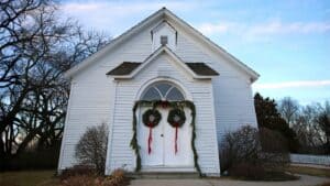 White church building decorated with Christmas wreaths on the front doors