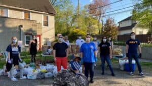 Volunteers stand outdoors beside tables and bags of food prepared for community distribution.